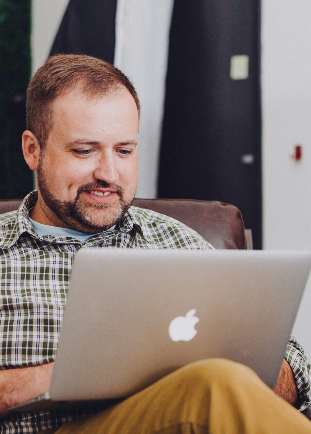 Man in blue checkered shirt on apple macbook while sitting in an office