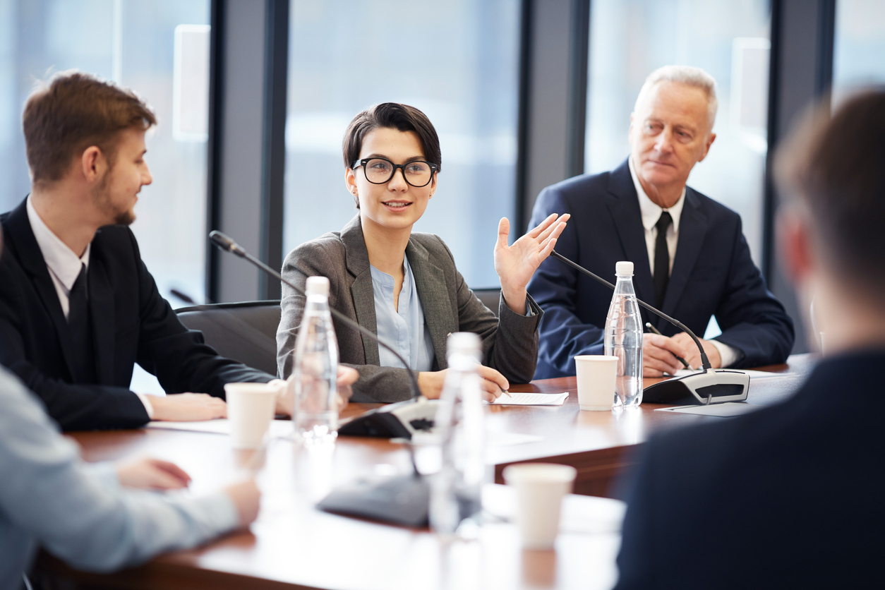 Portrait of young businesswoman speaking to microphone during group discussion in conference room