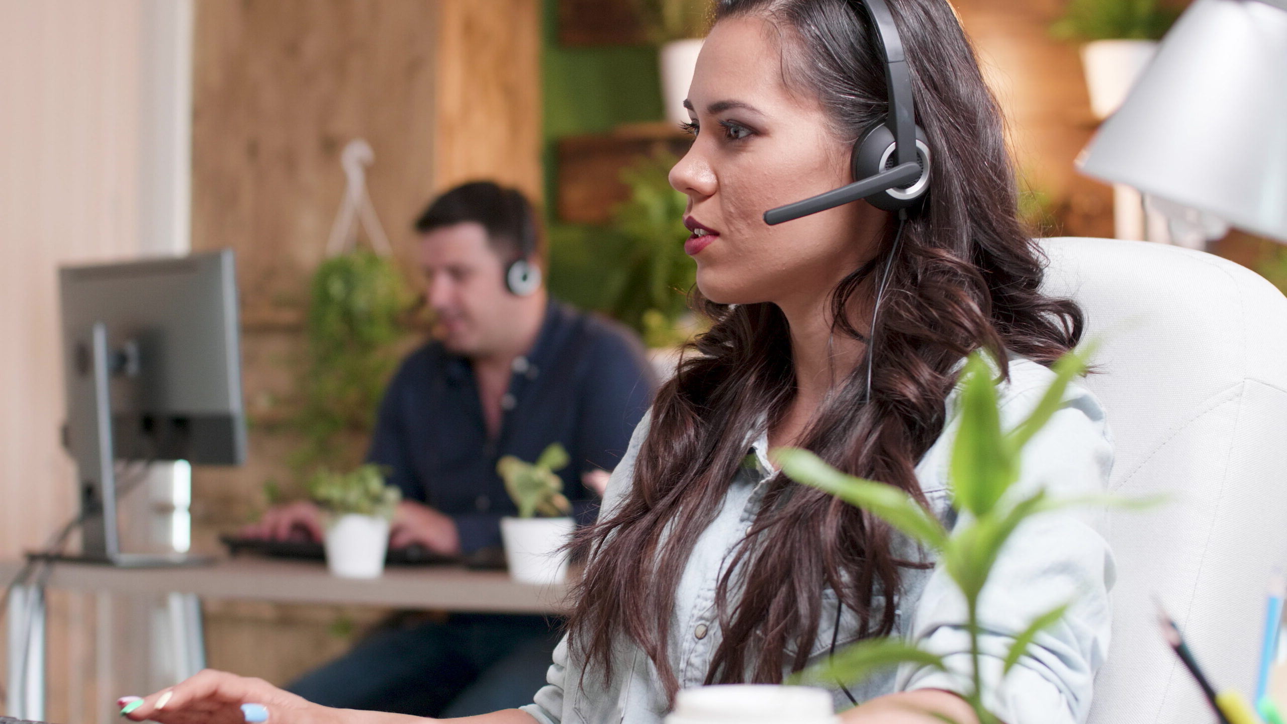 Young support customer woman talking into headset microphone with call center customer while working in startup company office. Caucasian female consultant providing telemarketing service
