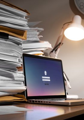 a laptop on a desk with a stack of papers