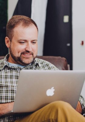 Homme en chemise bleue à carreaux, assis dans un bureau, sur son macbook.