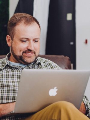 Mann in blau kariertem Hemd an einem Apple Macbook, während er in einem Büro sitzt