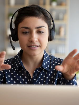 Woman wearing wireless headset video conference calling on laptop