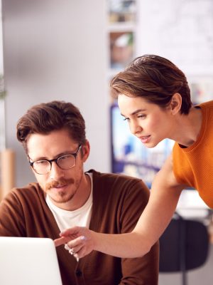 Mannelijke en vrouwelijke architecten op kantoor die aan bureau op laptop werken en plannen bekijken