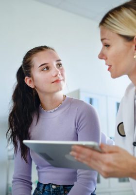 Junge Ärztin, die einem Teenager in ihrem Büro die Diagnose erklärt.