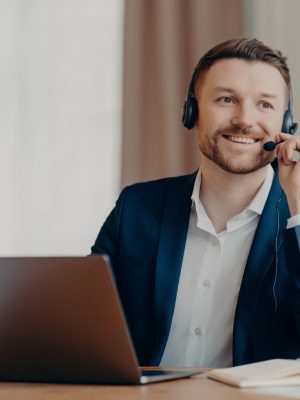 Foto van gelukkige mannelijke manager draagt headset werkt op laptop met behulp van Digtasoft pro