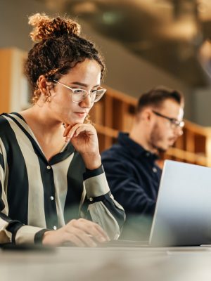 Portret van enthousiaste Latijns-Amerikaanse jonge vrouw die aan de computer werkt in een modern, helder kantoor. Zelfverzekerde Human Resources Agent glimlacht blij terwijl ze online samenwerkt met collega's.