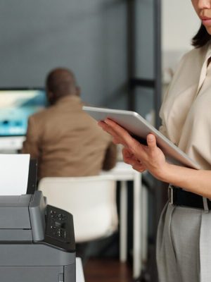 Focus on tablet held by businesswoman computing in office while standing by printer. Powered by Document Automation Solutions