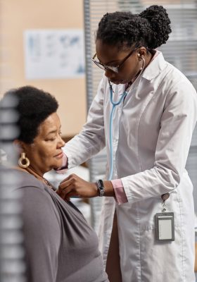 Vertical shot of focused African American female physician conducting auscultation for mature female patient during check up in hospital