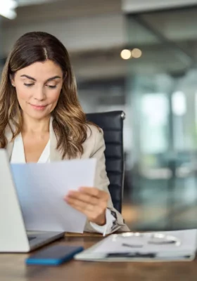 Impegnata donna d'affari di mezza età che lavora in ufficio con il computer portatile leggendo un documento. Donna matura manager avvocato che tiene carta relazione finanziaria seduto alla scrivania in ufficio. Spazio copia