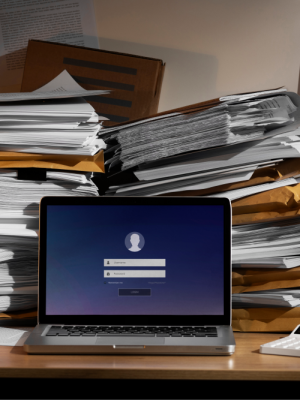 a laptop on a desk with stacks of papers